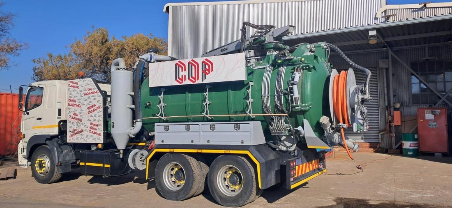 Green vacuum truck with hose reels outside an industrial workshop